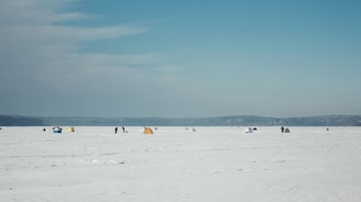 A panoramic view of a frozen lake dotted with colorful ice fishing tents under a dramatic cloudy sky.