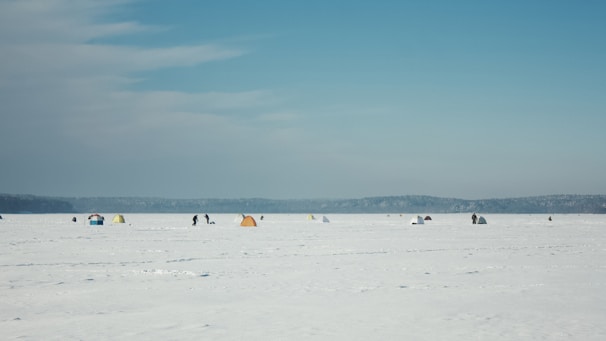 A panoramic view of a frozen lake dotted with colorful ice fishing tents under a dramatic cloudy sky.