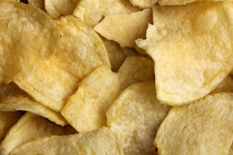 A close-up view of crispy, golden potato chips overlapping each other, displaying their textured and slightly oily surface.