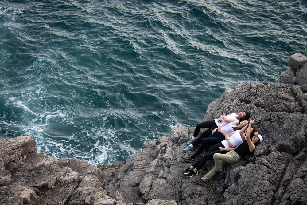 woman in white tank top and black leggings sitting on rock by the sea during daytime