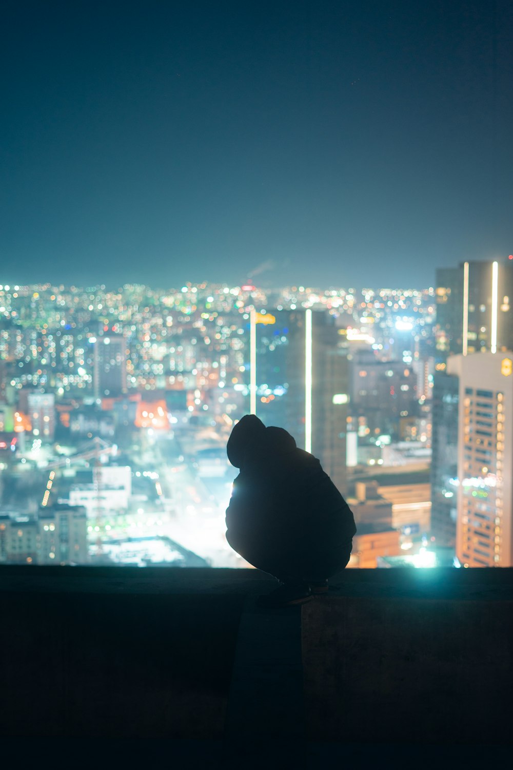 silhouette of person sitting on window looking at city buildings during night time