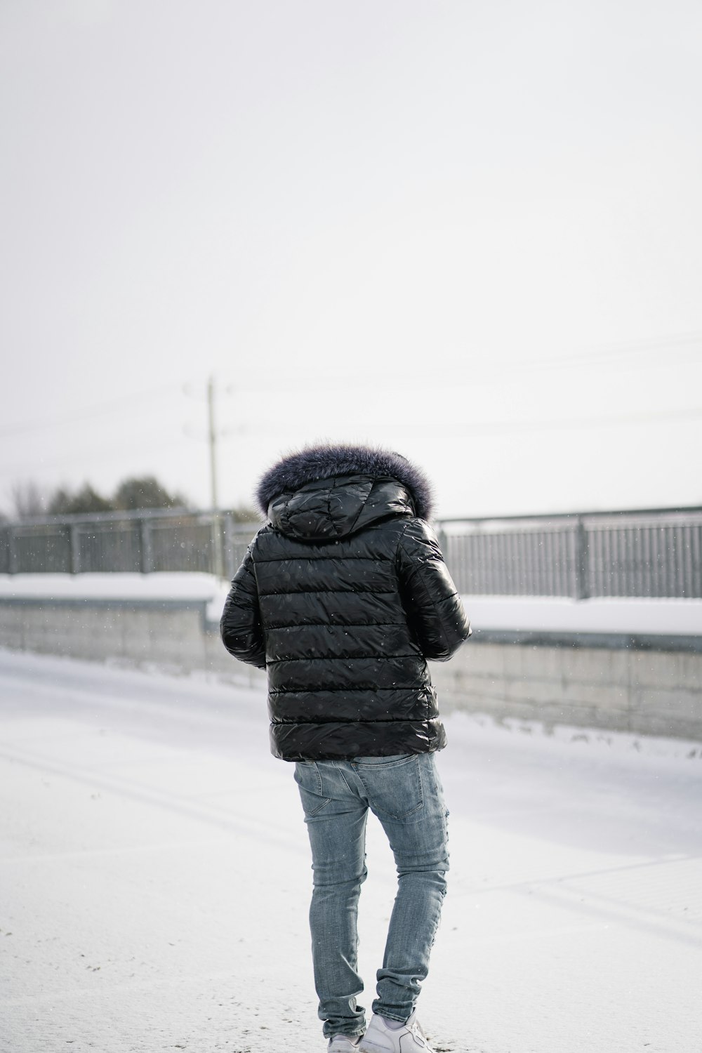 黒のパーカージャケットとブルーデニムジーンズを着た人が昼間、雪に覆われた地面に立つ