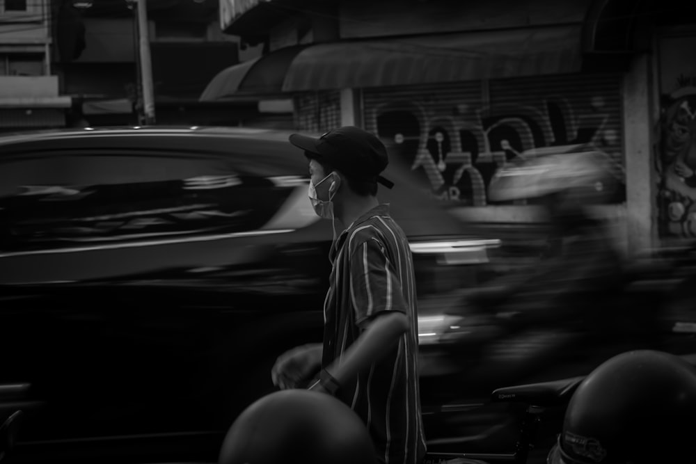 grayscale photo of man in jacket and hat sitting on car