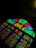 A colorful stained glass window featuring geometric patterns with vivid colors. The design includes various shapes in red, blue, green, and yellow with a dark background that accentuates the brightness of the glass.