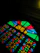 A colorful stained glass window featuring geometric patterns with vivid colors. The design includes various shapes in red, blue, green, and yellow with a dark background that accentuates the brightness of the glass.