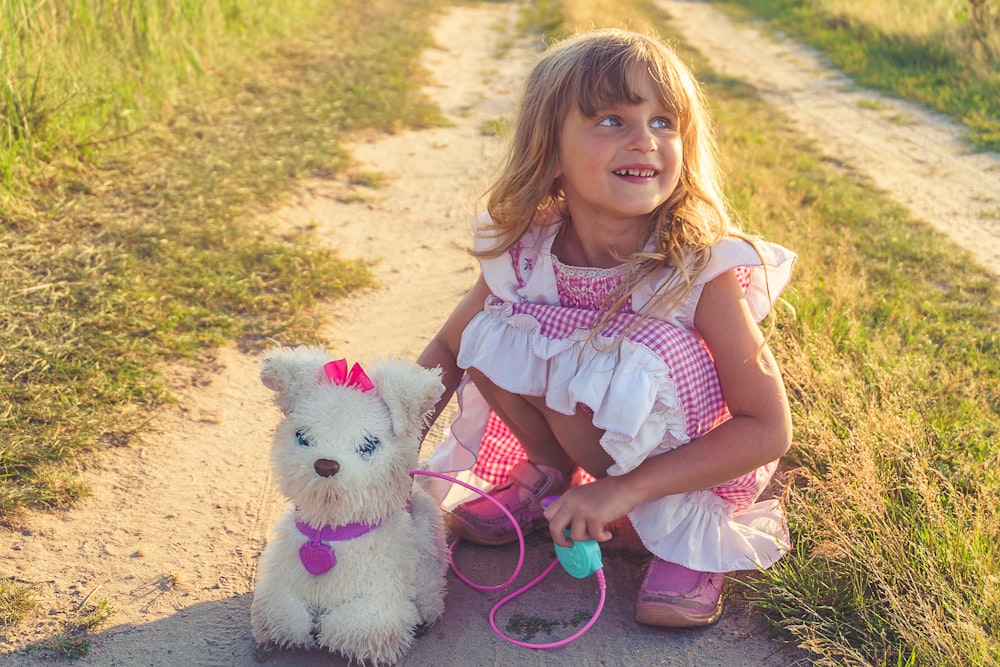 girl in pink and white dress holding white dog plush toy