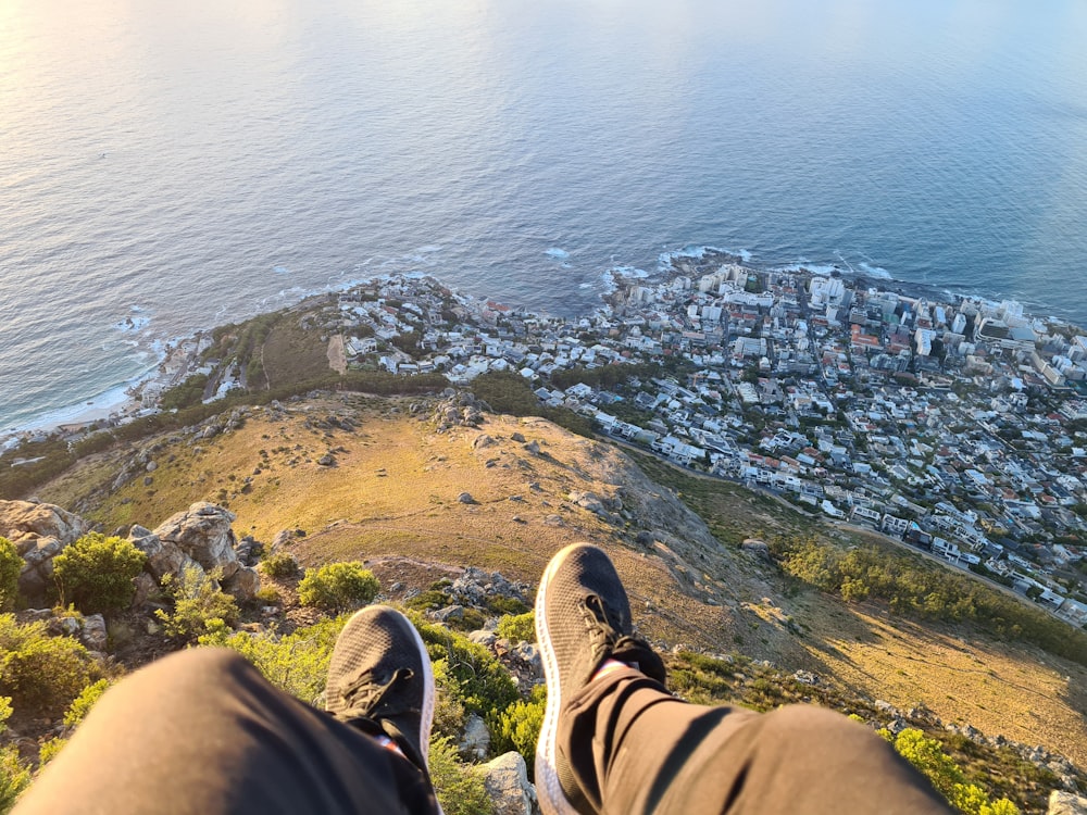 person in brown pants and black shoes sitting on brown rock near body of water during