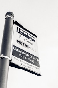 A black and white image of a bus stop sign for Littlehaven Station on Rusper Road. It provides directions towards North Heath, Hospital, and Town Centre.