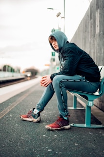 man in black hoodie and blue denim jeans sitting on gray concrete bench during daytime