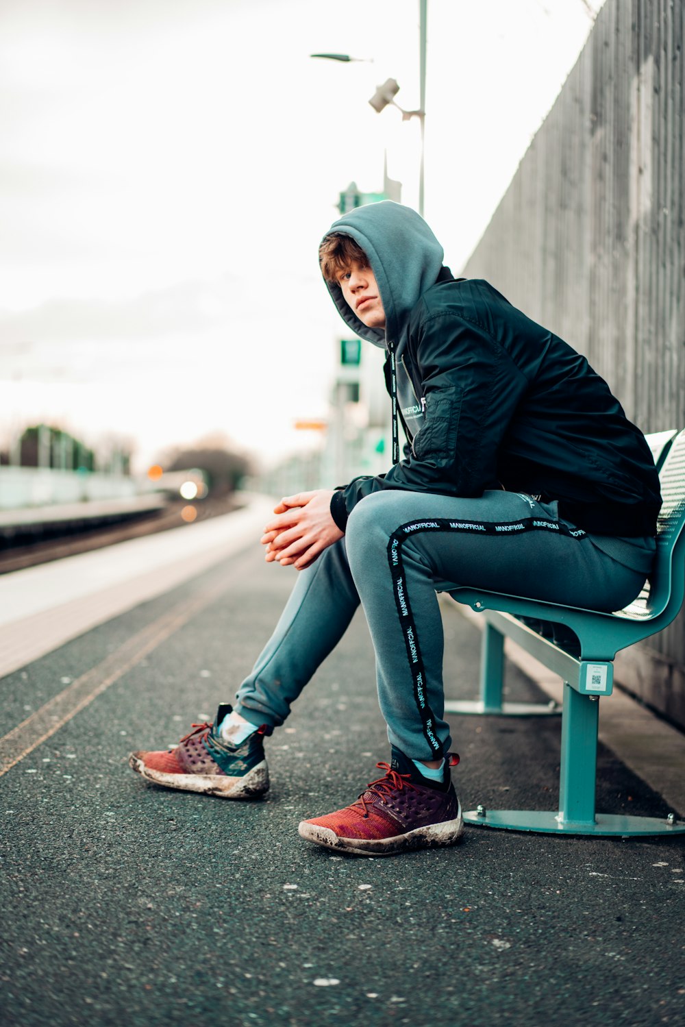 man in black hoodie and blue denim jeans sitting on gray concrete bench during daytime