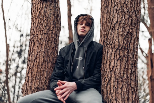 man in black zip up jacket sitting on tree trunk