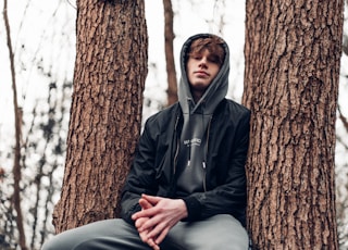 man in black zip up jacket sitting on tree trunk