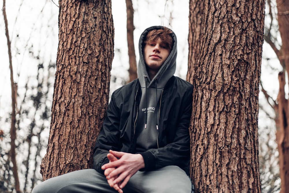 man in black zip up jacket sitting on tree trunk