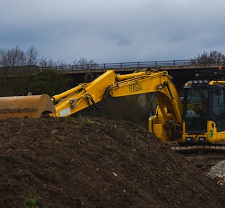 yellow excavator on brown soil under white clouds during daytime