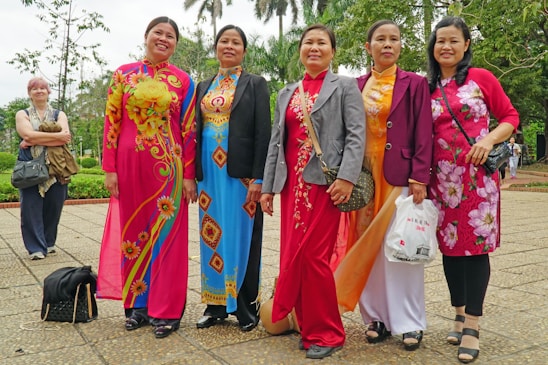 A diverse group of women from different cultures standing together outdoors, smiling and holding hands in solidarity.
