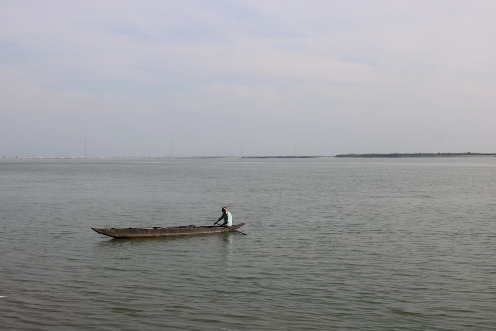 man in black shirt and black pants standing on brown wooden boat on sea during daytime