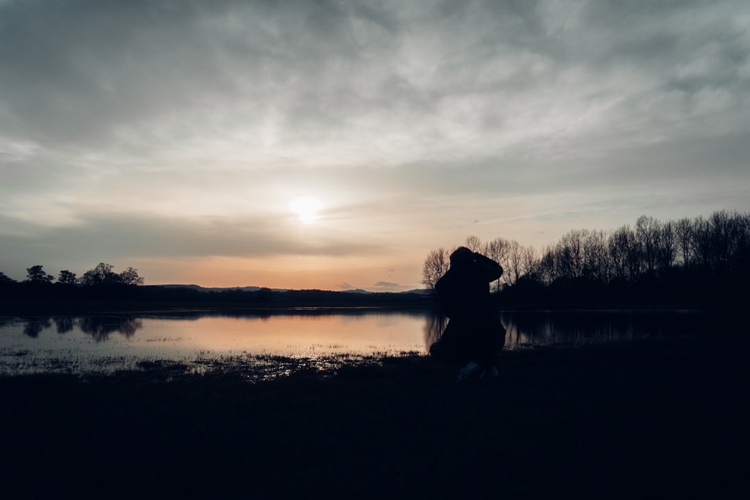 silhouette of person standing near body of water during sunset
