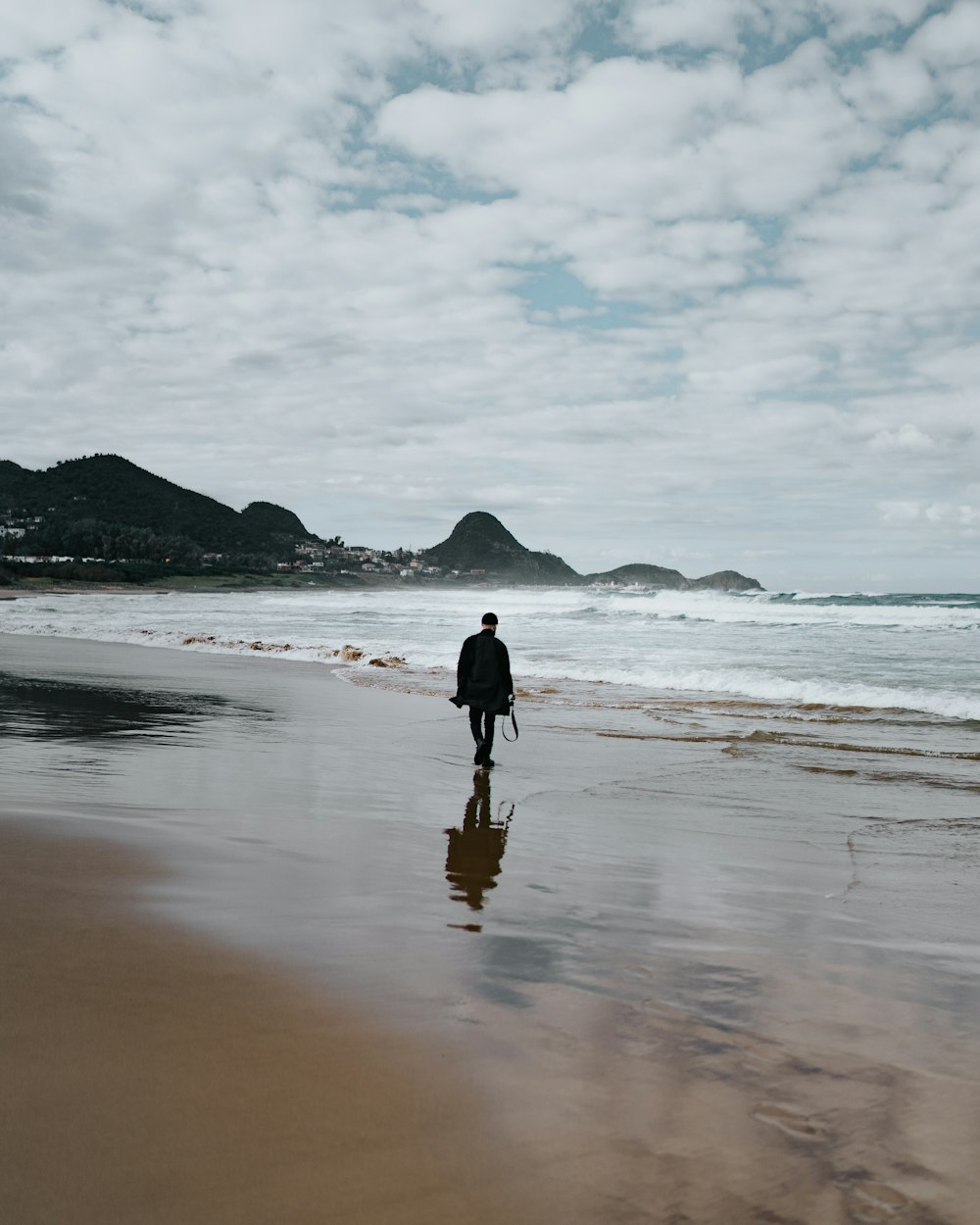 Persona in giacca nera che cammina sulla spiaggia durante il giorno