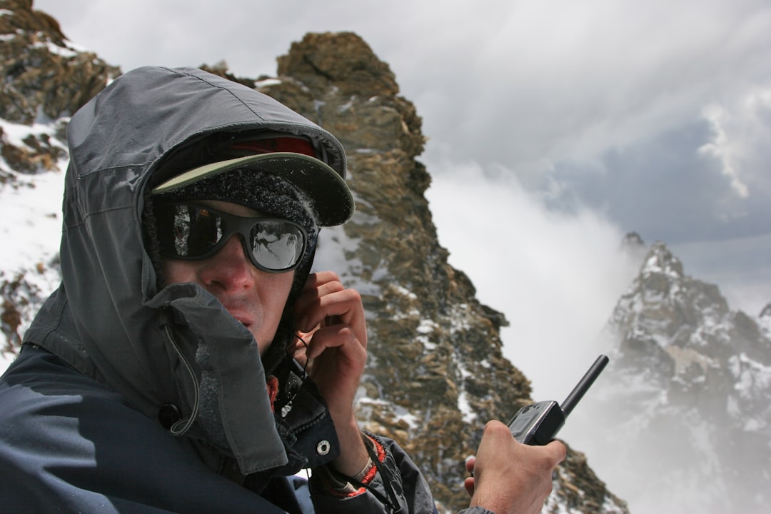 man in black jacket holding black smartphone, A climber calling rescue team by satellite phone
