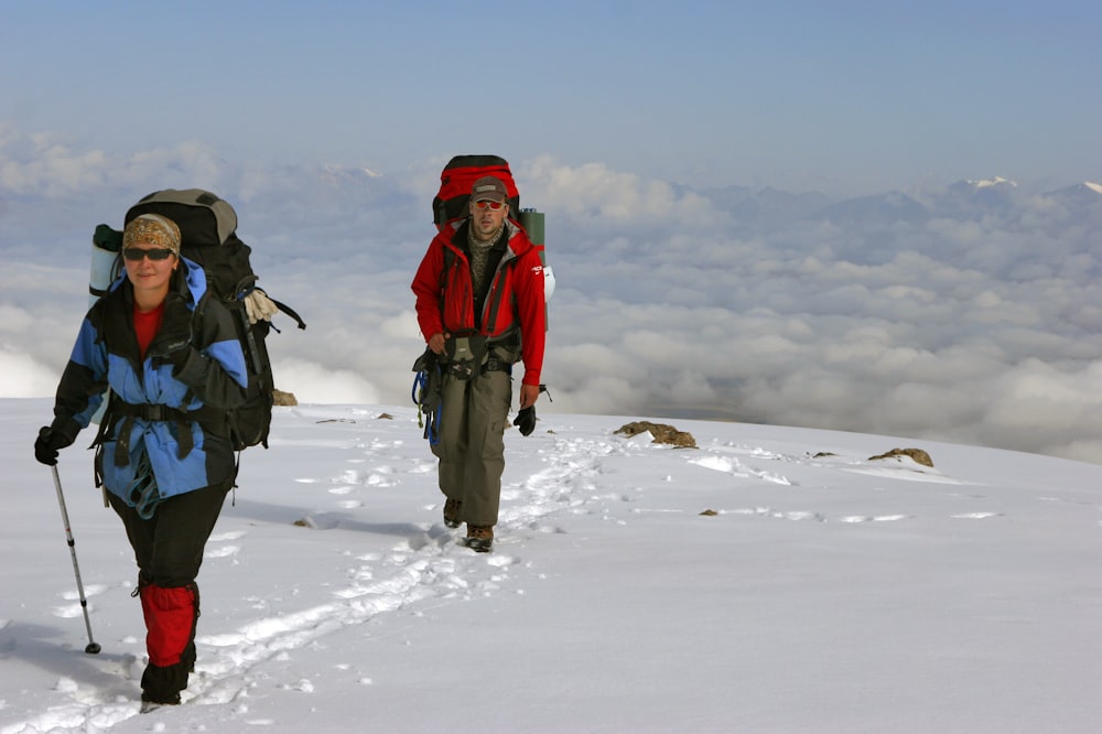 woman in red jacket and black pants carrying black backpack on snow covered field during daytime