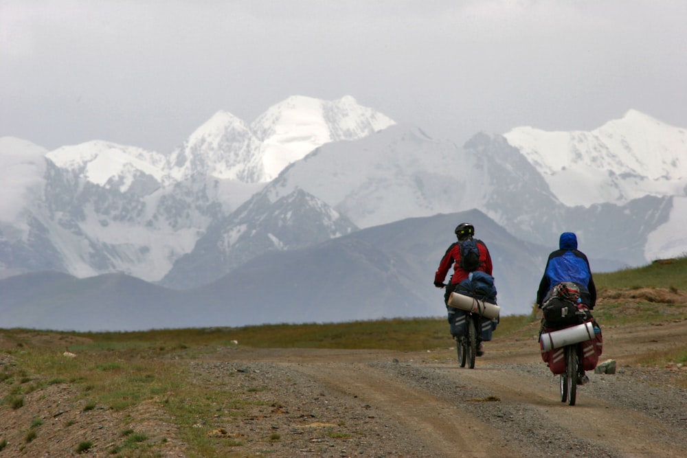 people riding on bicycles on dirt road near snow covered mountain during daytime