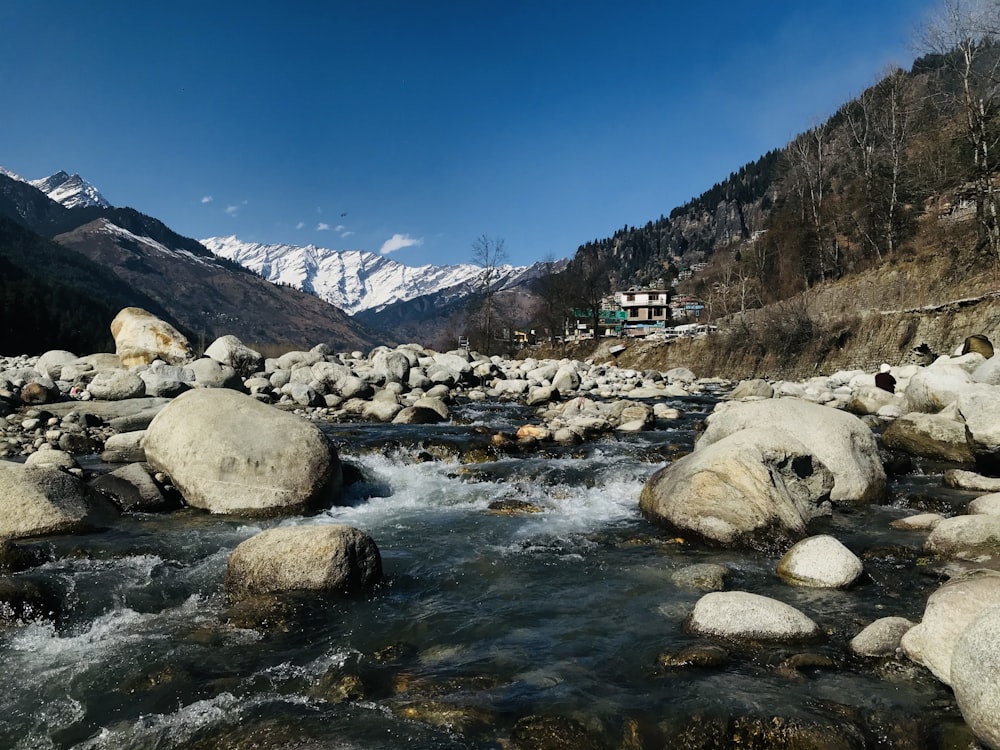 rocky river with rocks and mountains in distance under blue sky during daytime