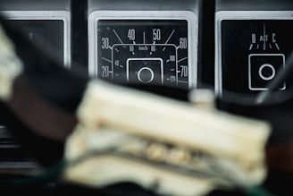 A close-up view of vintage car speedometers displaying various measurement units. The focus is on the central speedometer, which is labeled with numbers indicating kilometers per hour. Nearby, there are additional panel indicators with circular designs.