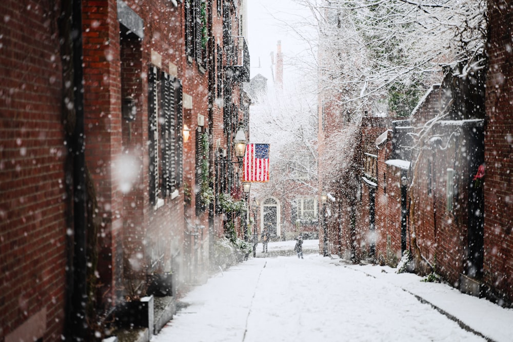 snow covered road between brown concrete buildings during daytime