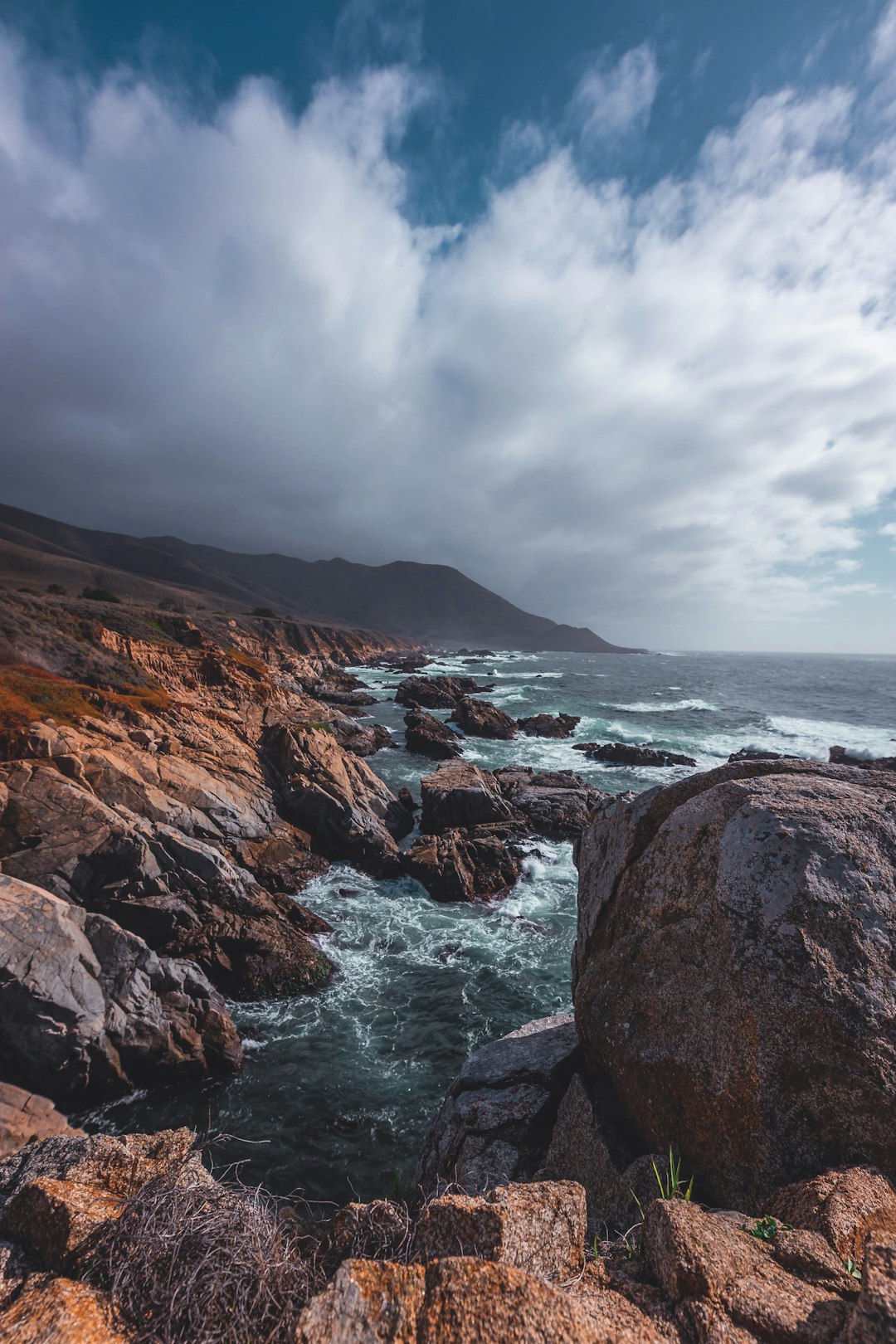 brown rock formation beside body of water under cloudy sky during daytime