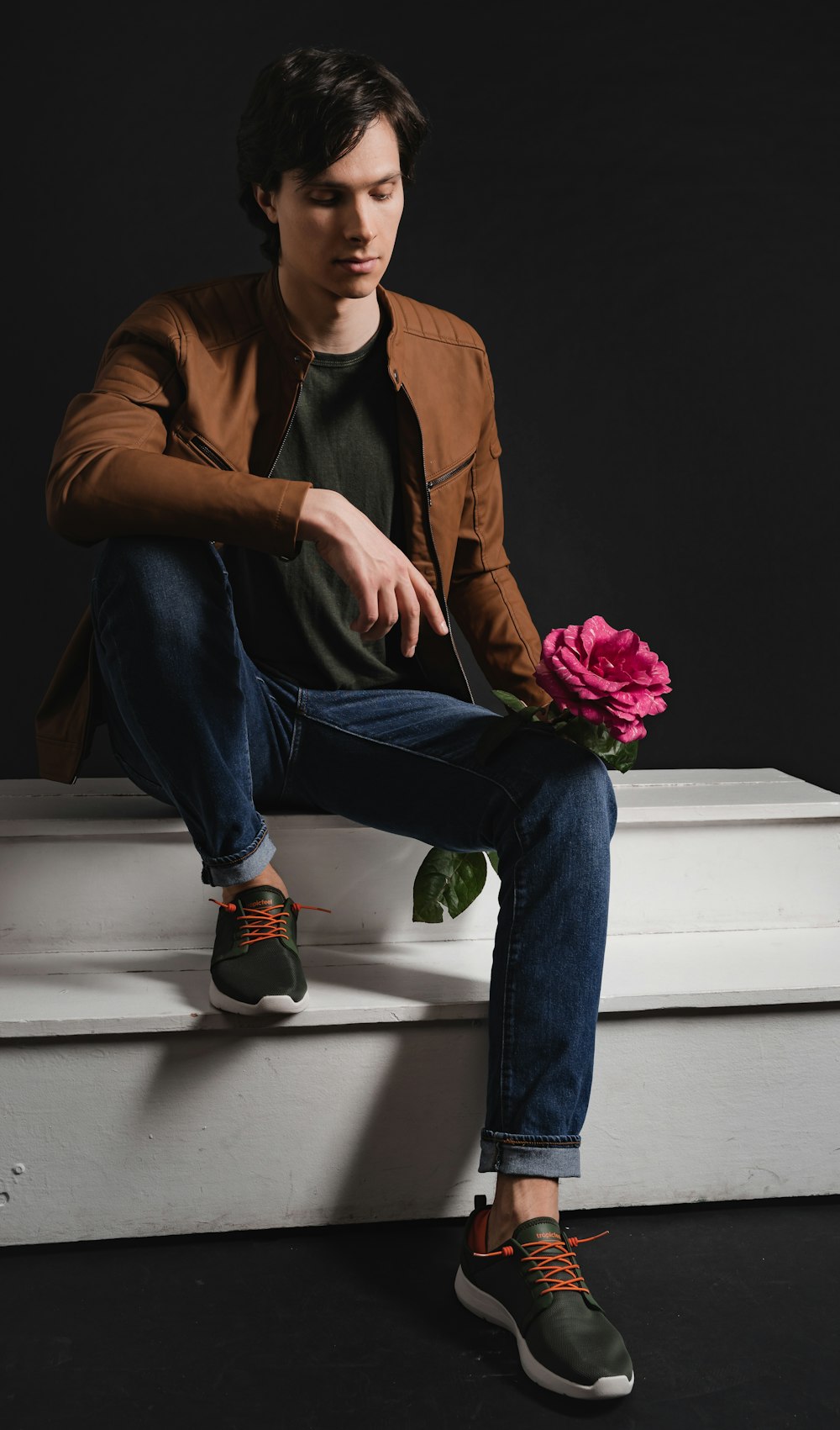 woman in brown leather jacket and blue denim jeans sitting on white concrete stairs