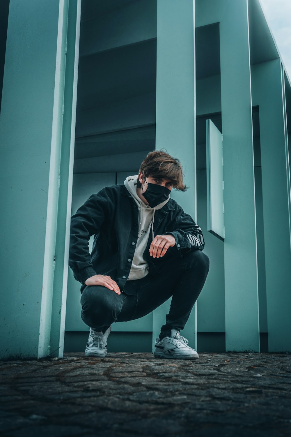 Homme en veste noire et pantalon noir assis sur une porte en bois bleu