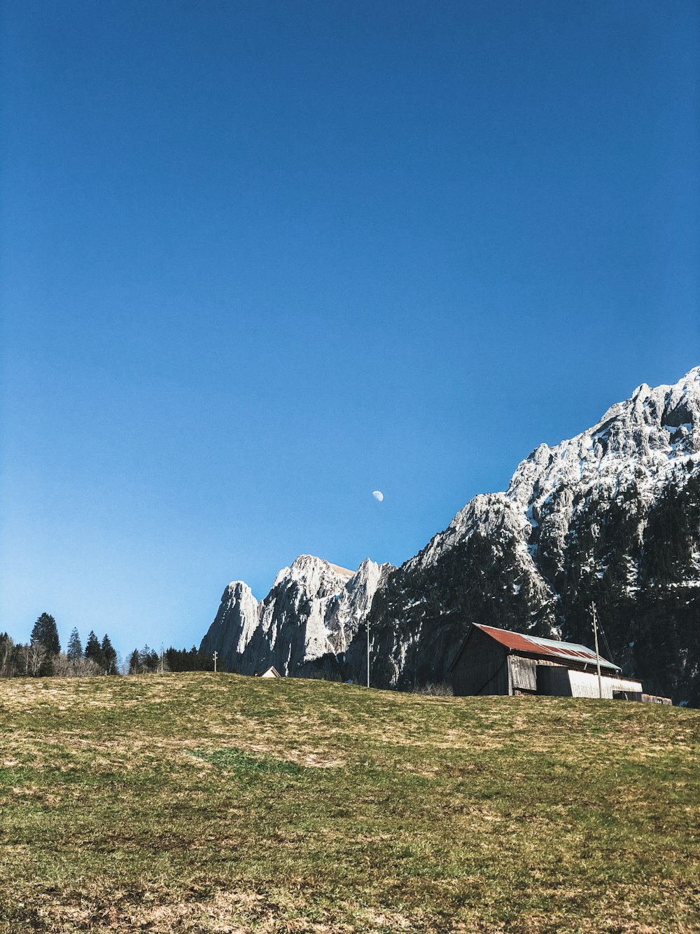 maison blanche et brune sur le champ d’herbe verte près de la montagne rocheuse grise sous le ciel bleu pendant