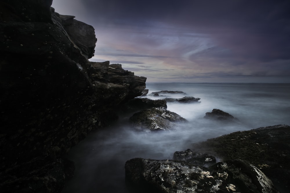 ocean waves crashing on rocks under gray clouds