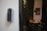 A smart digital lock with a keypad is mounted on a white wall. In the background, there is a blurred view of a dining area with a table and chairs, and some wall art is partially visible.
