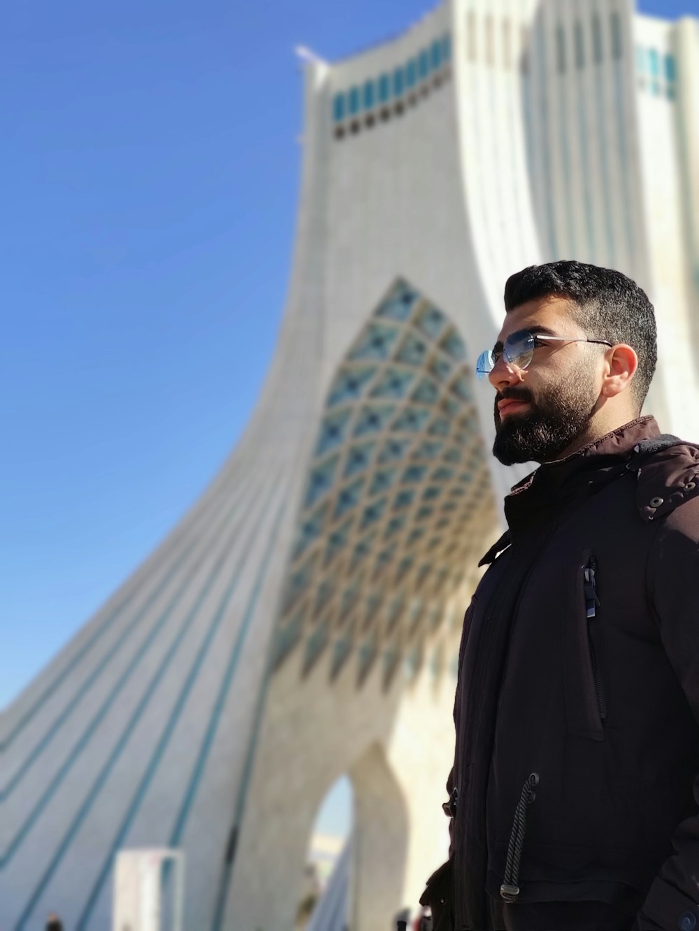 man in black jacket standing near white concrete building during daytime