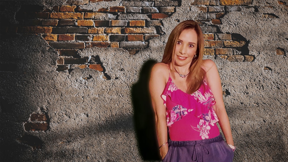 girl in pink tank top and black skirt standing beside brown brick wall