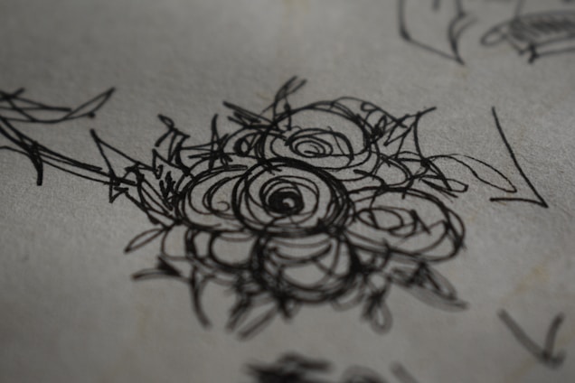 A close-up of a hand sketching an elegant floral invitation design on textured paper.