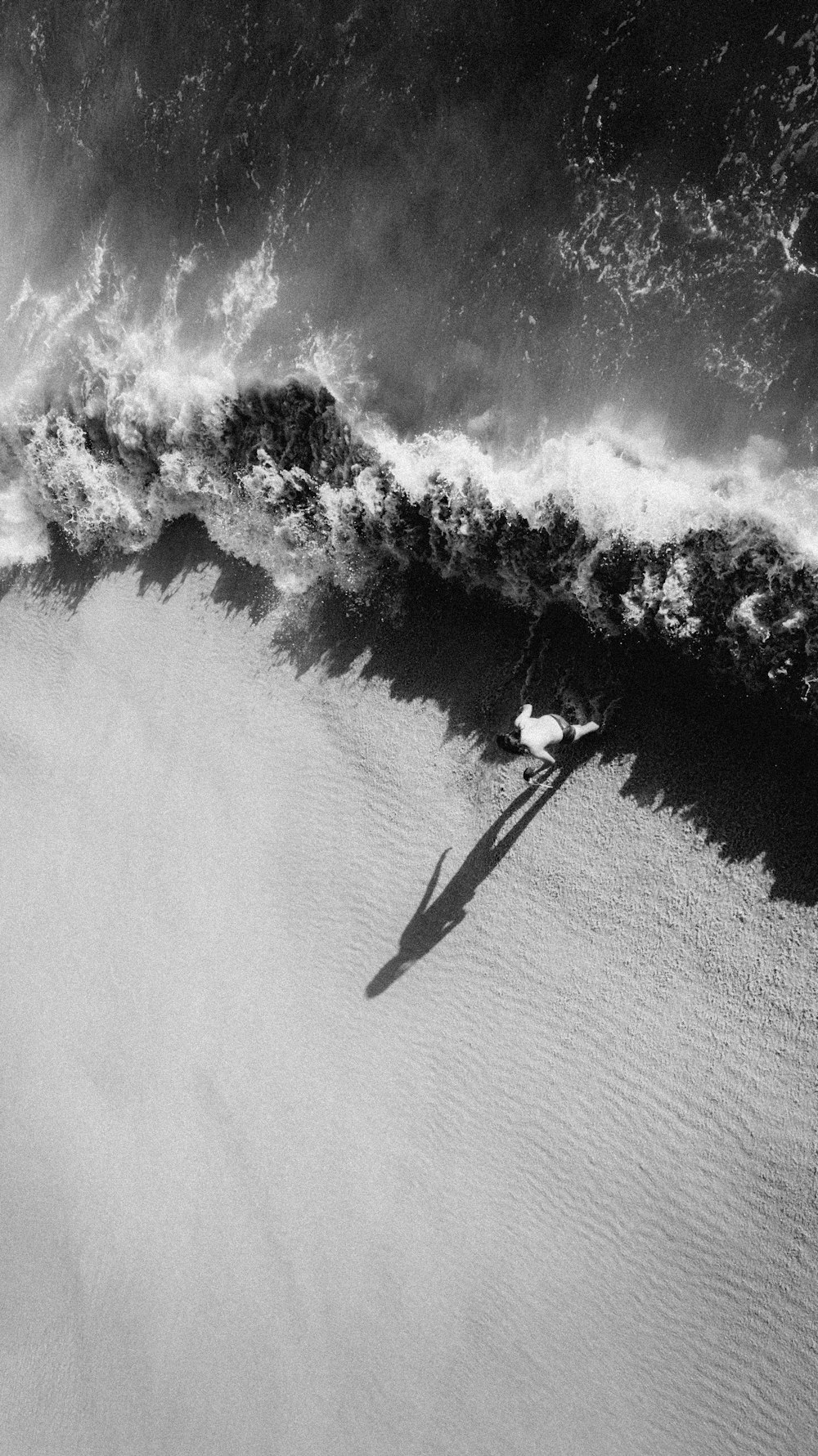 Photo en niveaux de gris d’un homme en veste noire et pantalon debout sur une planche de surf