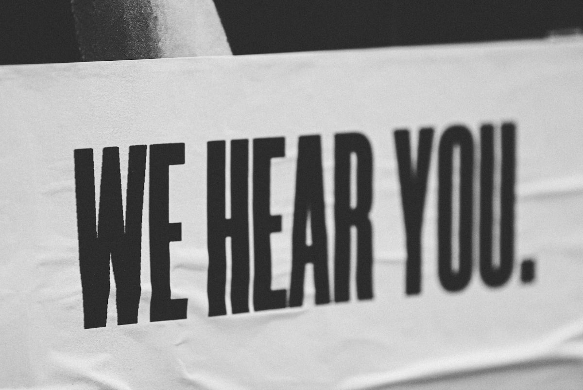 A black and white photo of a white banner with "We Hear You." printed in large, capitalized, block letters.