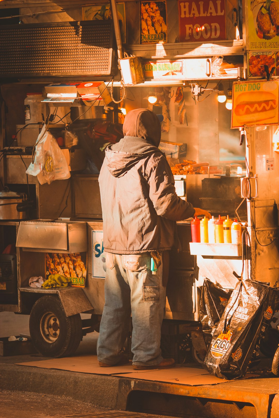 man in gray hoodie and pants standing in front of food stall
