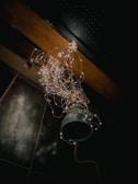 A hanging industrial-style light fixture adorned with a cascade of fairy lights. The lights create a warm, enchanting glow against a dark background, highlighting the rustic texture of the metal fixture and the wooden beam it is attached to.