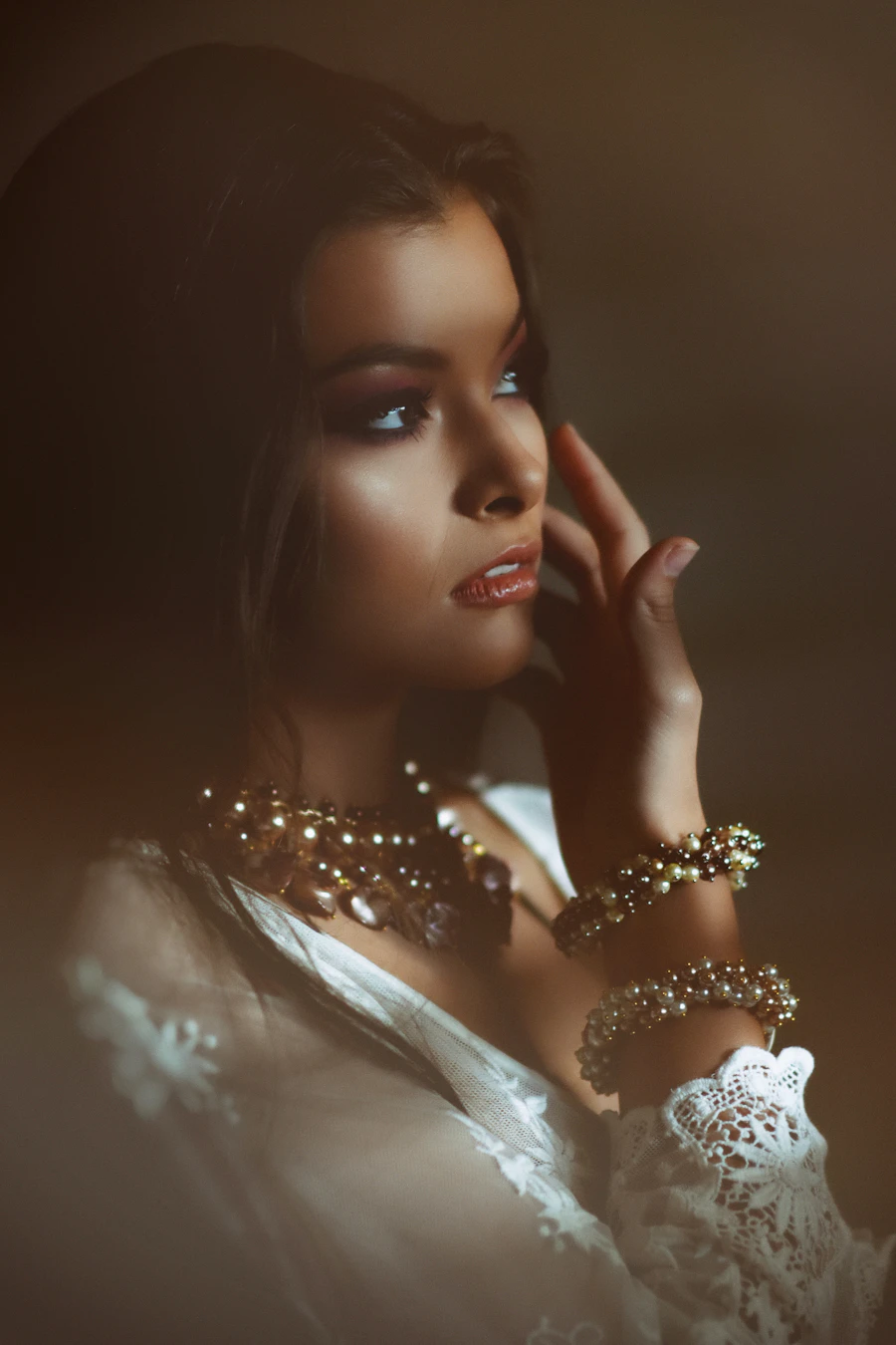 Adult woman in warm light wearing layered pearl and gold necklaces and bracelets