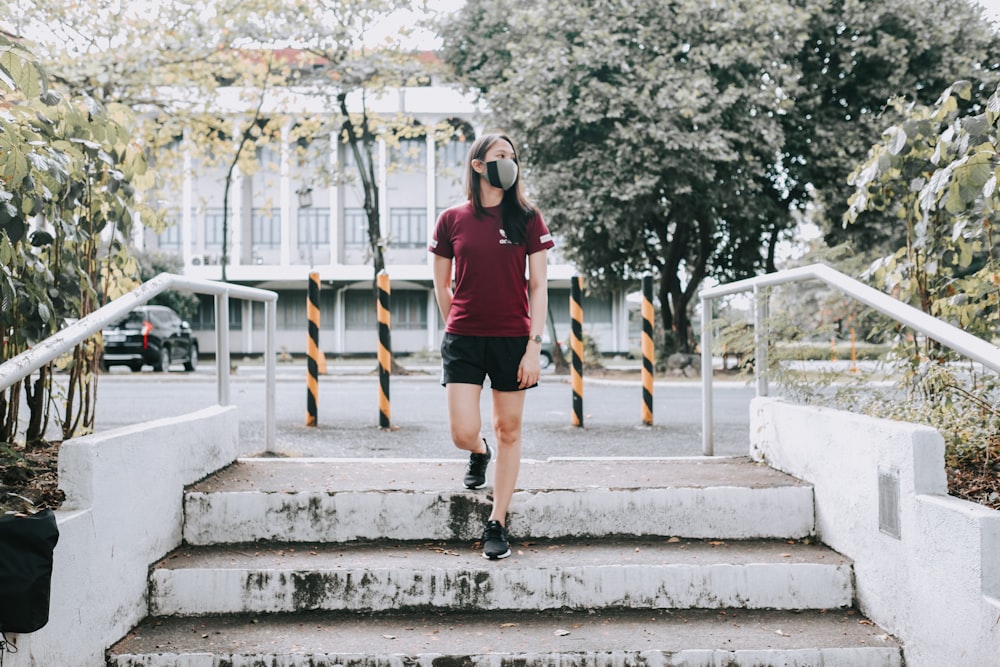 woman in red crew neck t-shirt and black shorts standing on gray concrete stairs during