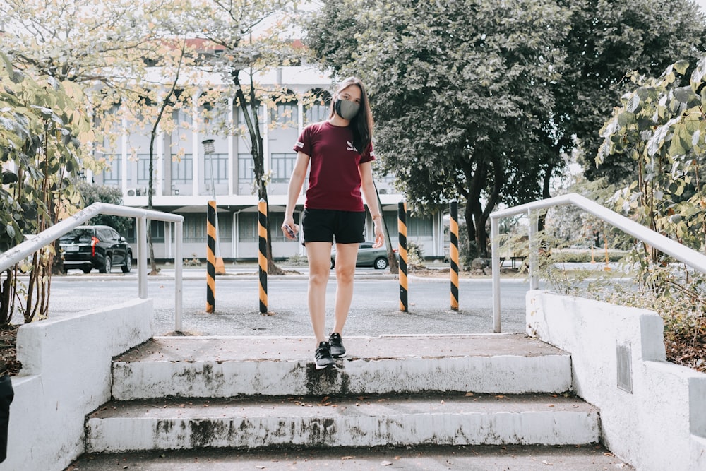 Mujer con camiseta sin mangas roja y pantalones cortos negros de pie en escaleras de hormigón gris durante el día