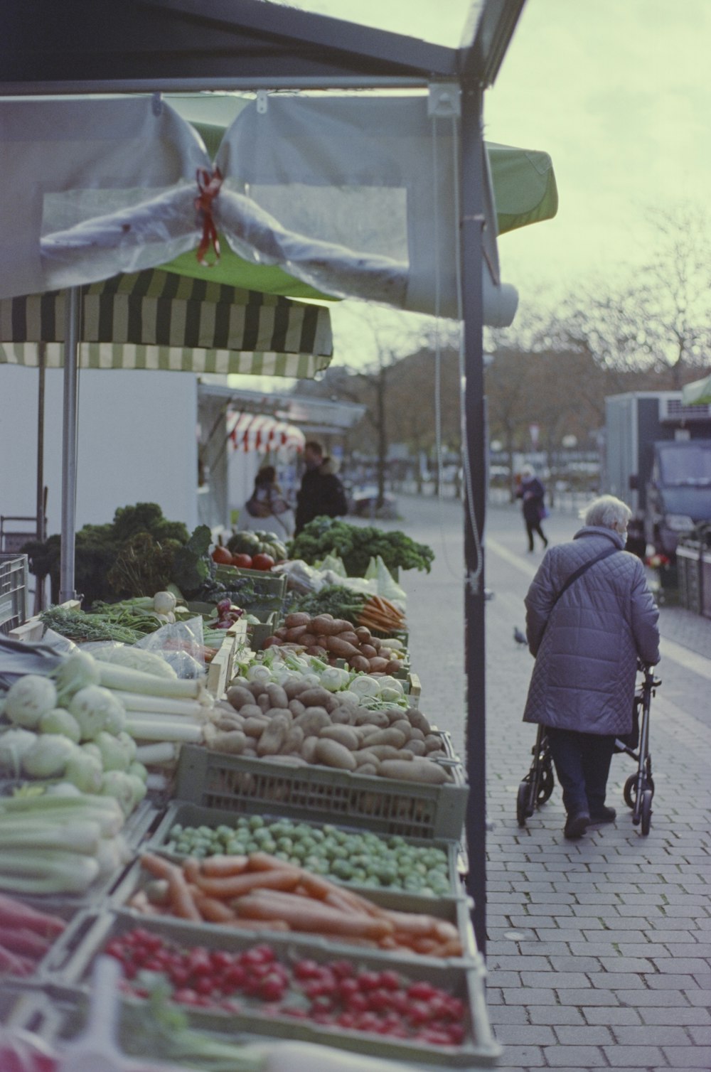 hombre con chaqueta negra de pie frente a un puesto de verduras