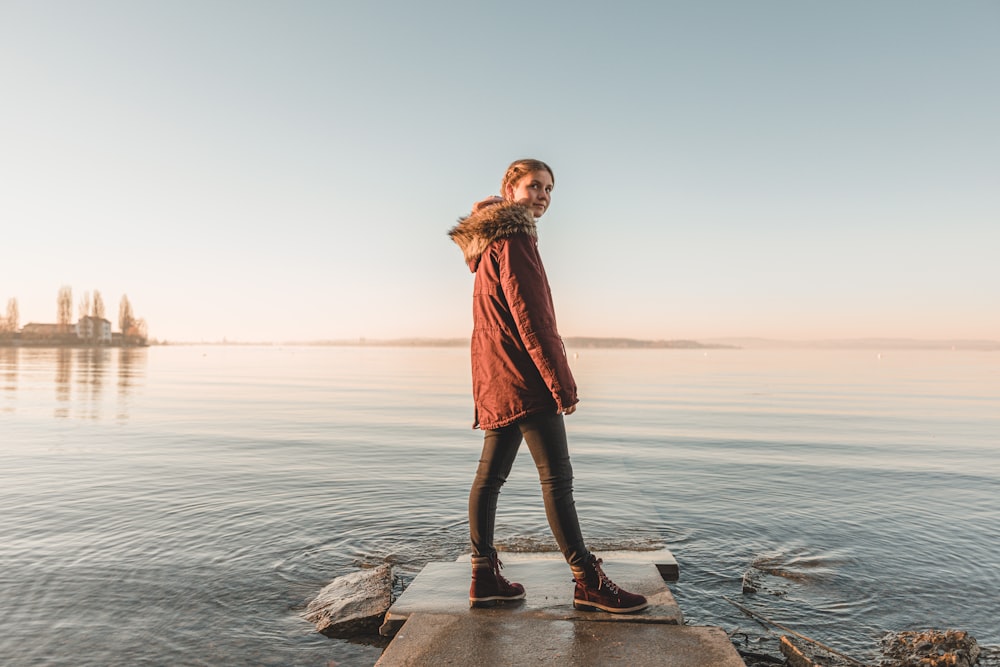 woman in red coat standing on rock near sea during daytime