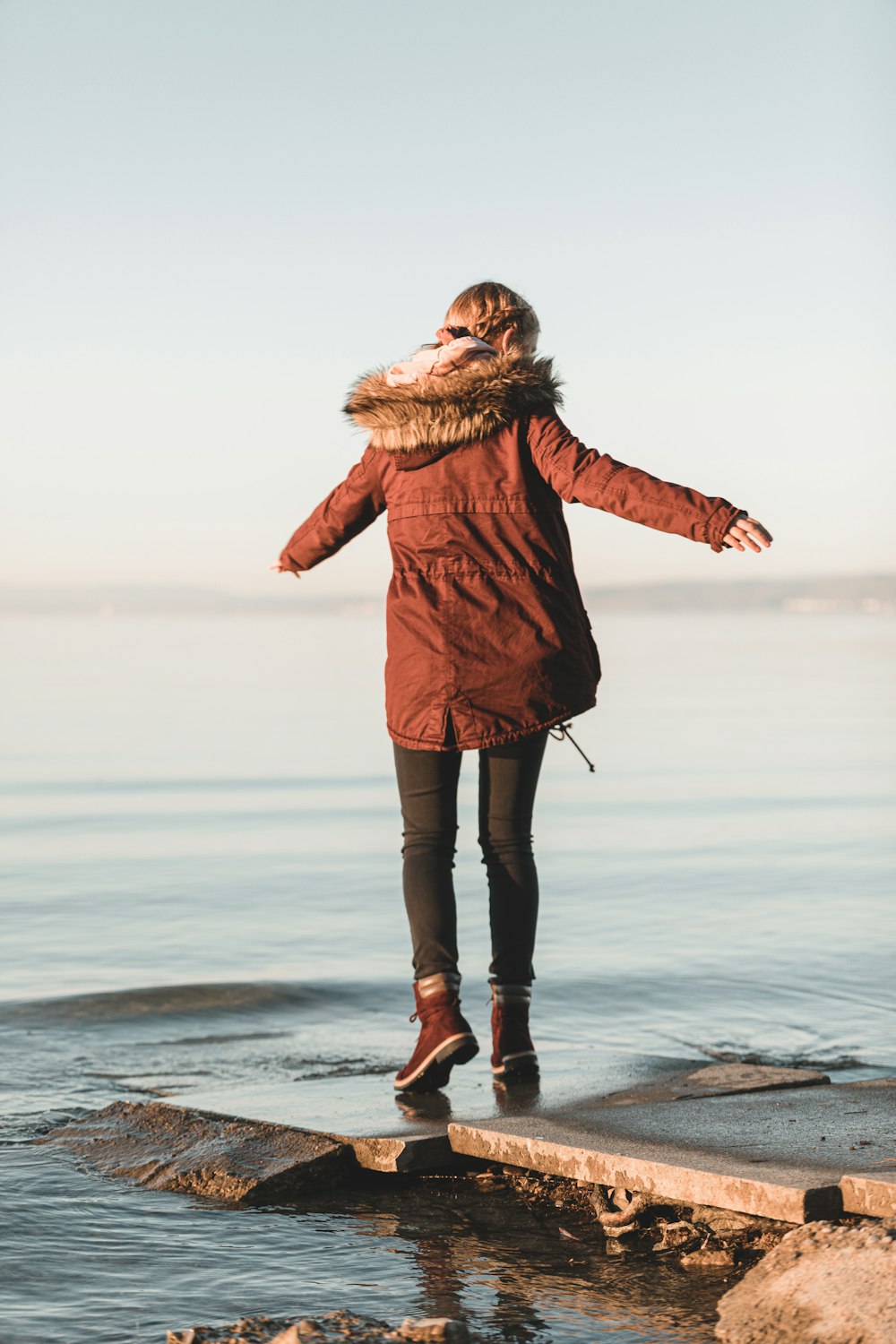 woman in brown coat standing on seashore during daytime