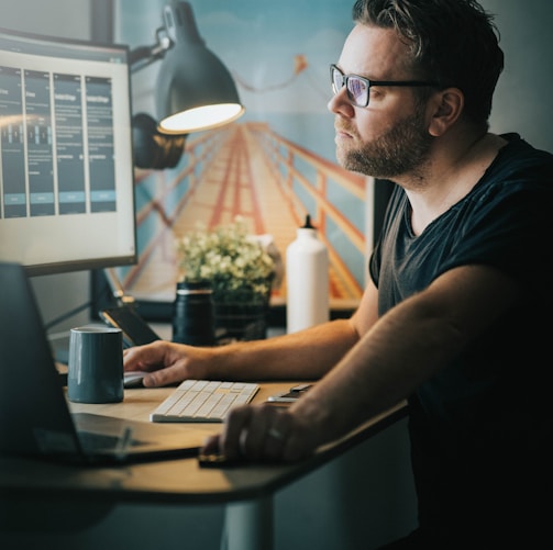 man in black crew neck t-shirt wearing black framed eyeglasses using computer