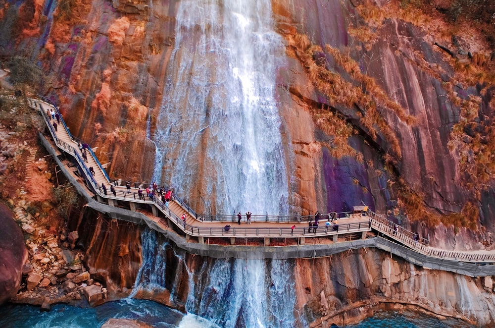 people walking on brown wooden bridge over waterfalls during daytime