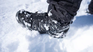 Close-up of navy blue winter socks with orange stitching peeking above a hiker's boot in snowy alpine terrain.